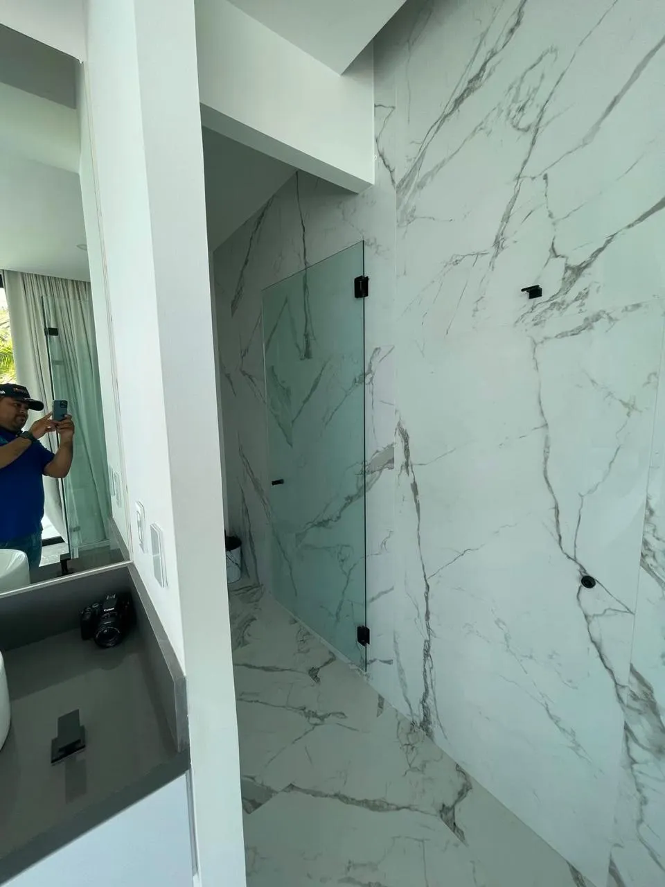 Puerta de cristal templado para regadera con muro de mármol blanco