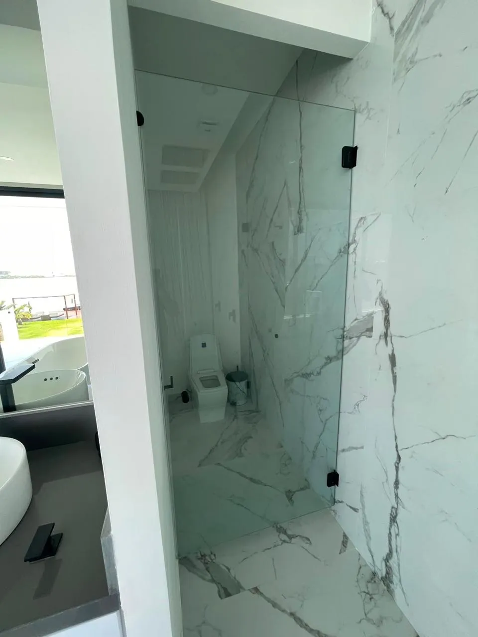 Cancel fijo de cristal templado que divide el sanitario en baño de mármol