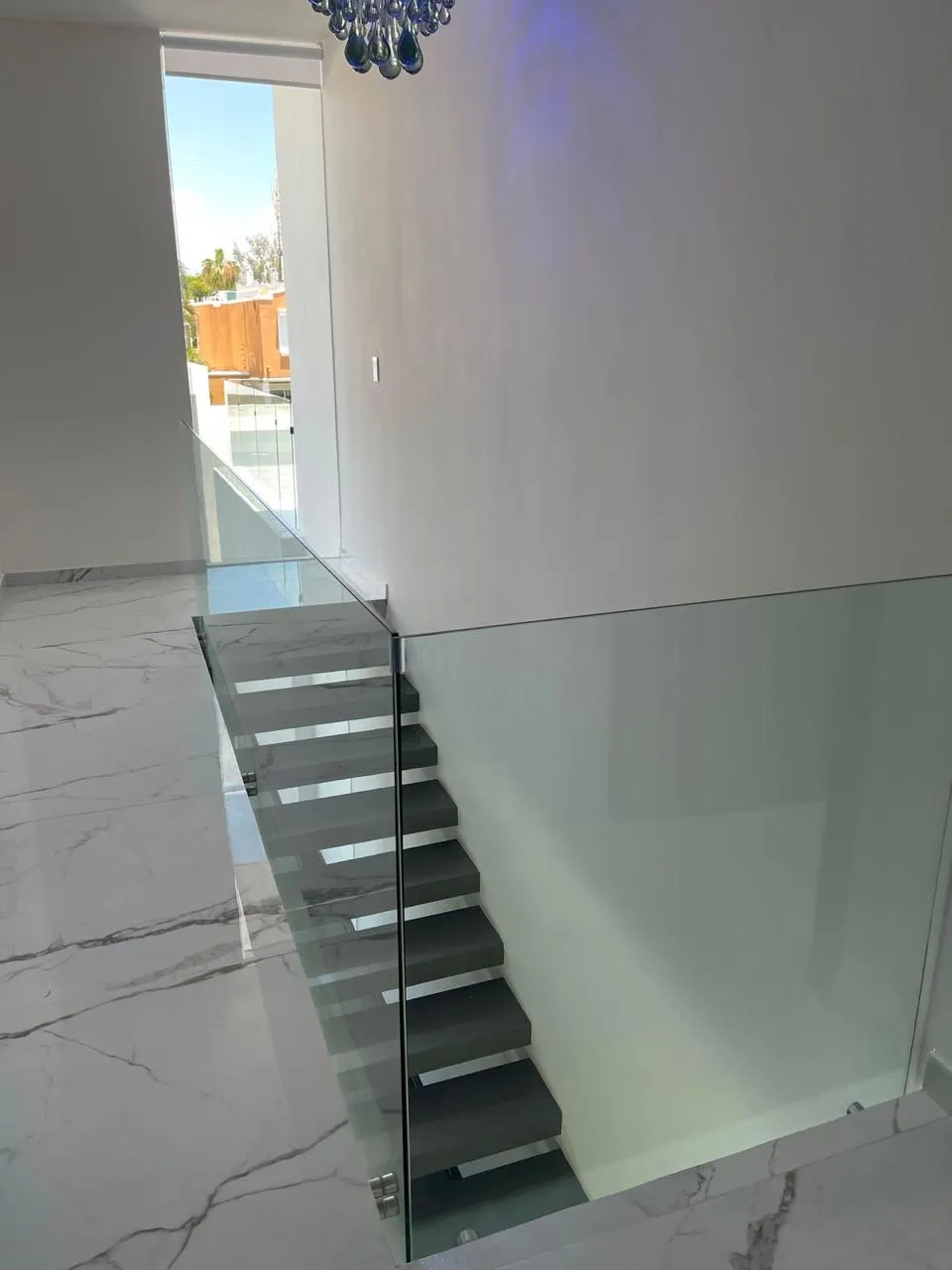 Barandal de cristal templado en escalera flotante sobre piso de mármol