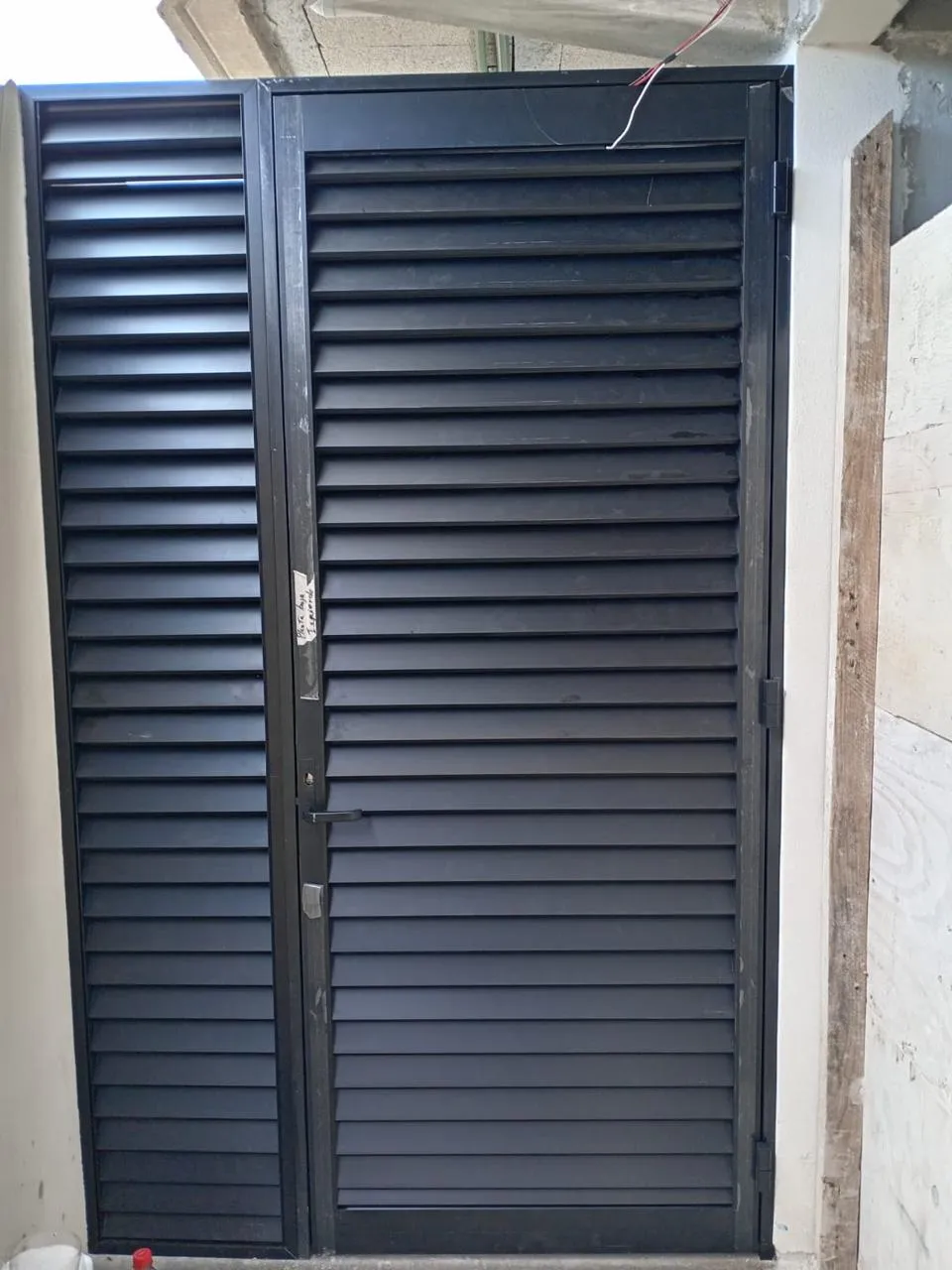 Puerta de persiana de aluminio negro con fijo de celosía