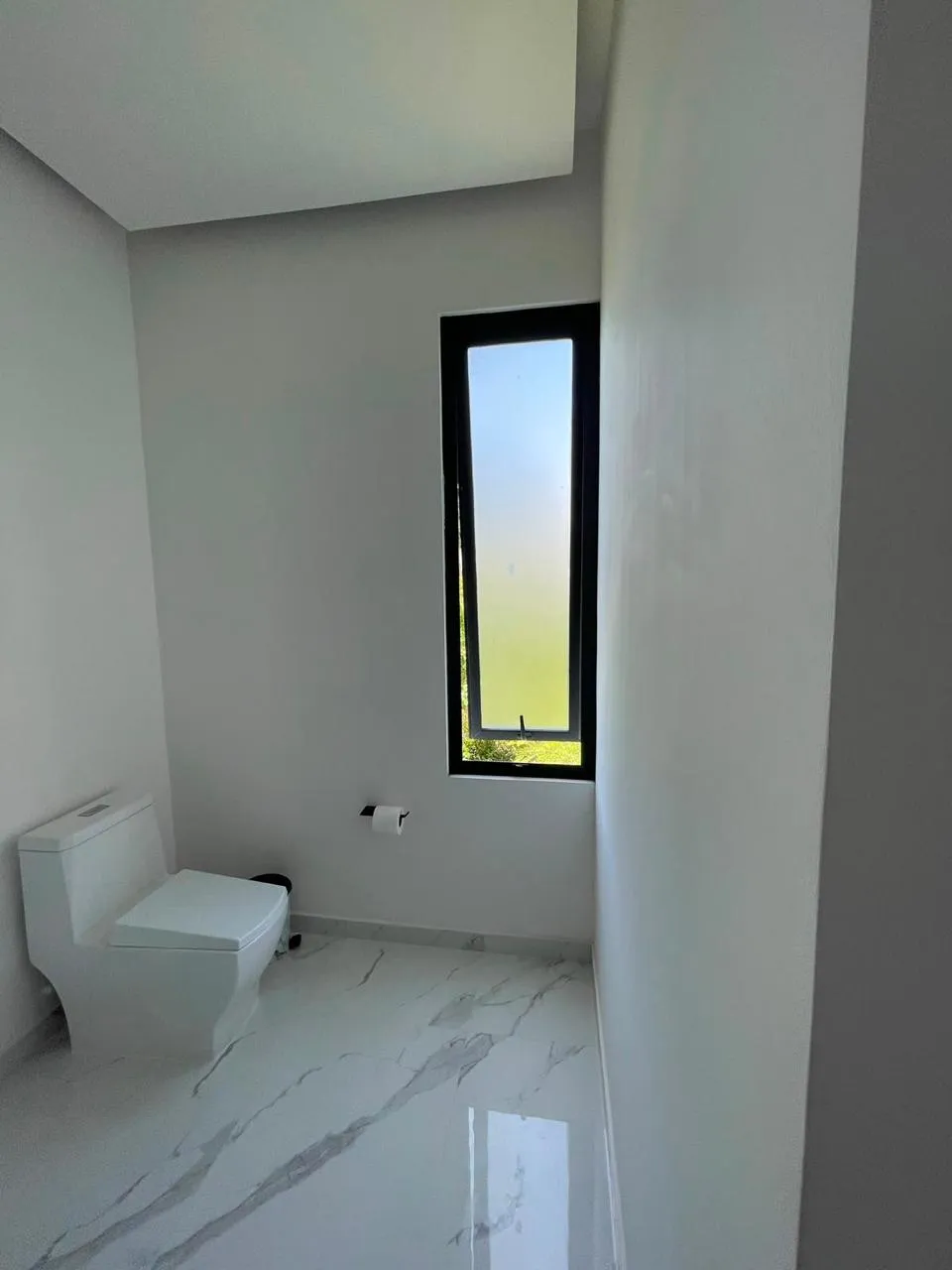 Ventana fija de aluminio negro en baño con piso de mármol