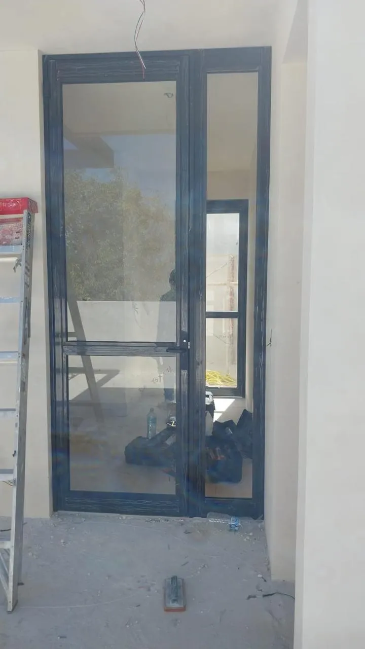 Puerta de aluminio negro con fijo lateral de cristal en obra