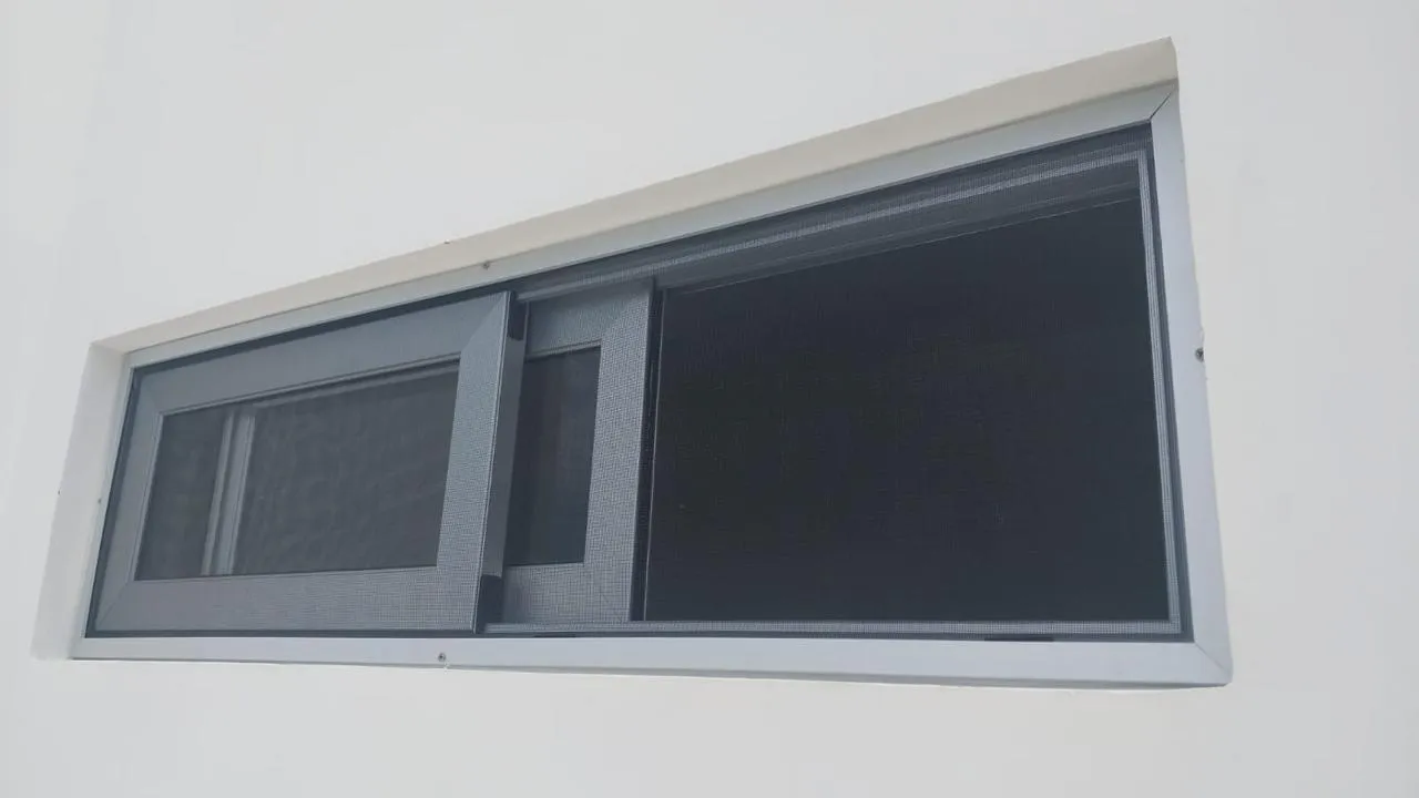 Ventana corrediza de aluminio blanco con mosquitero sobre muro blanco