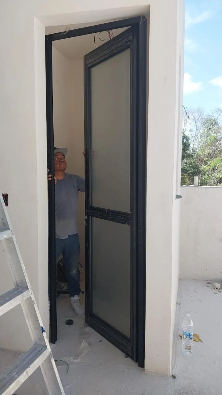 Puerta abatible de aluminio negro con cristal esmerilado en instalación