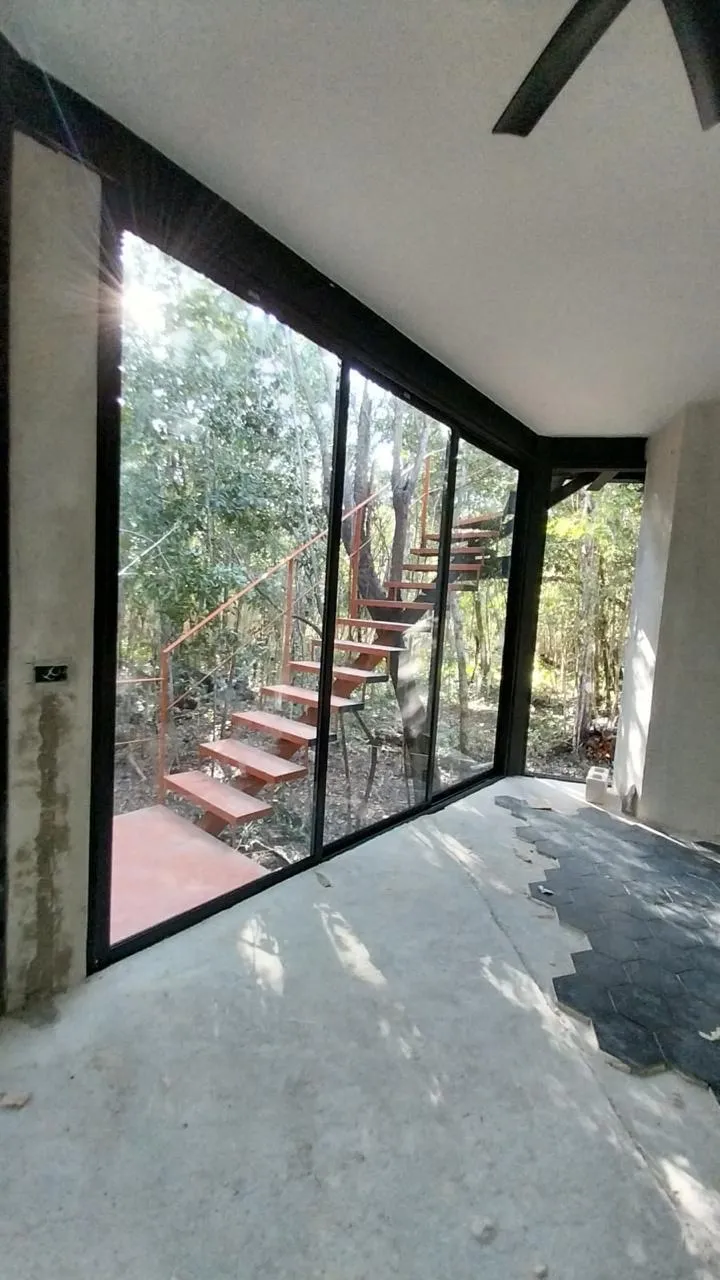 Ventanal fijo de aluminio negro con vista a escalera y selva