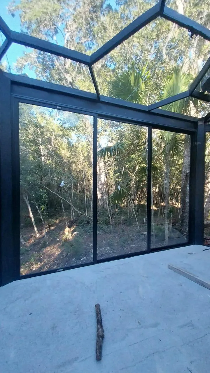 Pabellón acristalado de aluminio negro con techo de cristal en selva