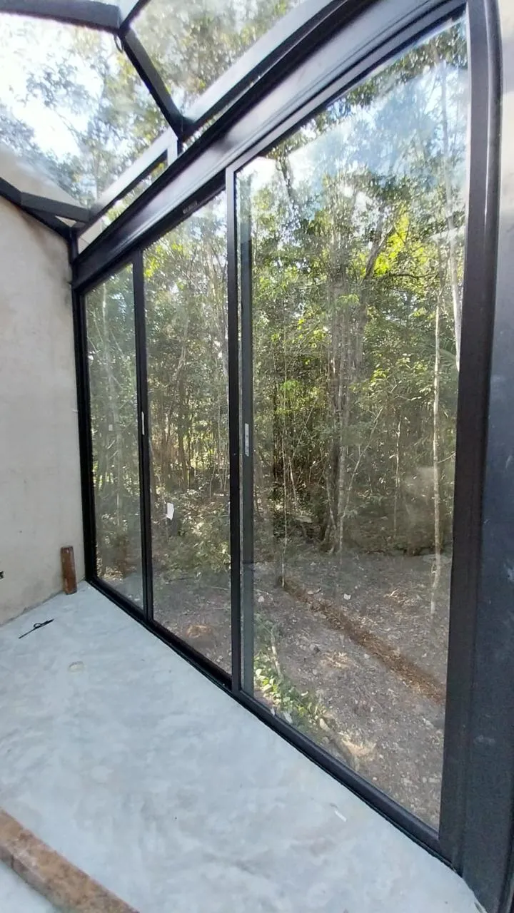 Pabellón de cristal con perfilería de aluminio negro en selva